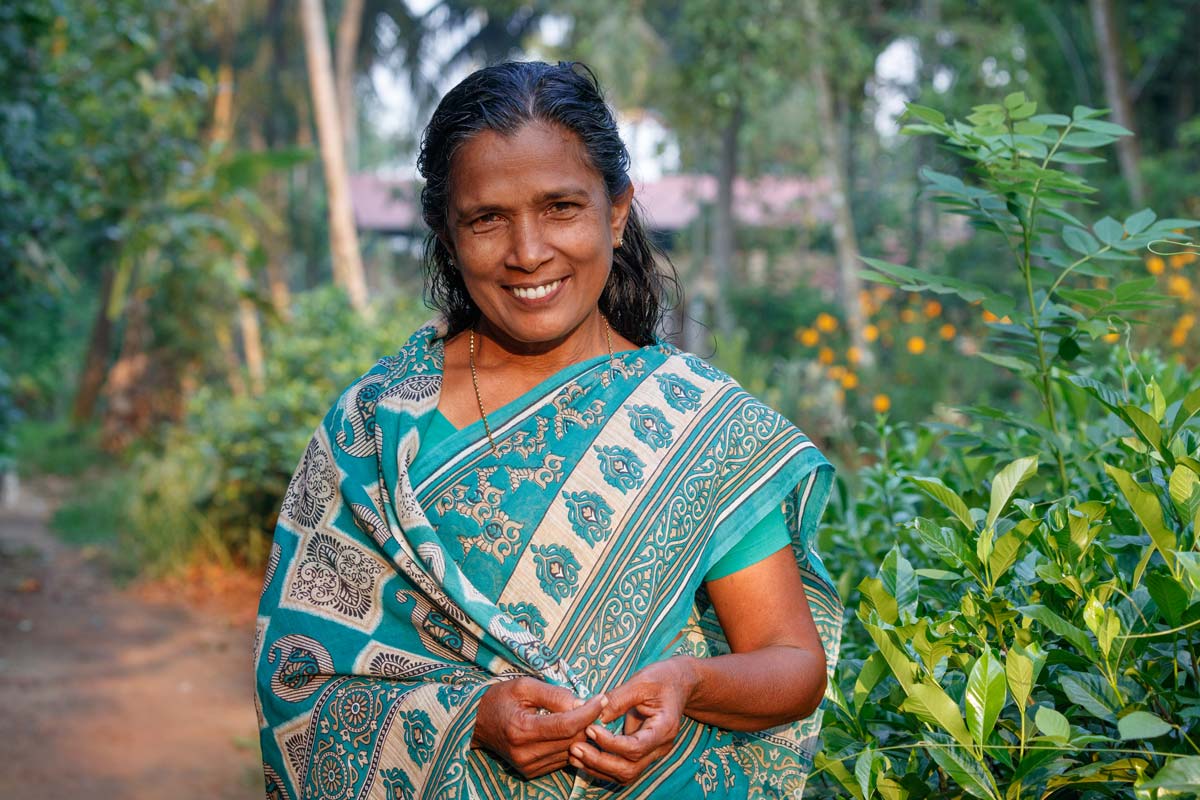 smiling woman wearing a beautiful scarf and standing before lush foliage in the background